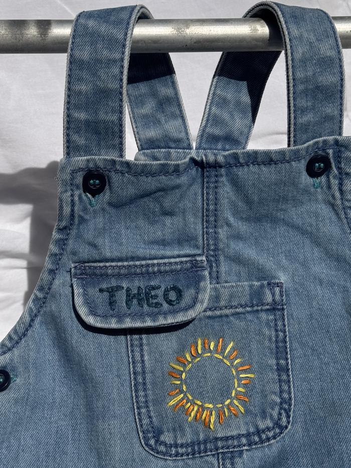 Denim dungarees with an embroidered name and hand-stitched sun motif