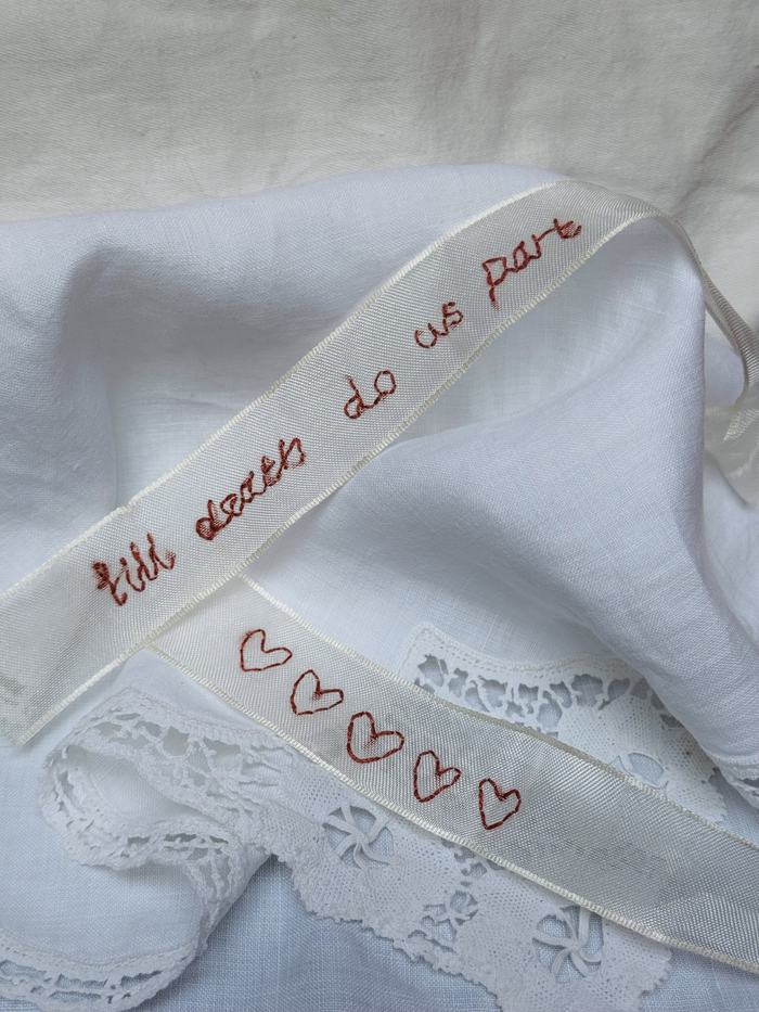 Embroidered ribbon with 'till death do us part' and hearts, laid over lace-trimmed linen